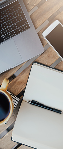 A laptop, a notebook, a pen, a cellphone and a cup of coffee over a desktop