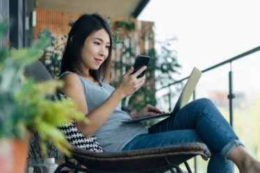 Mujer en una silla mirando su teléfono y computadora portátil